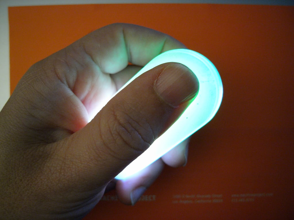 A hand holding Kombolói with a thumb against its rounded end as green and white light shines through the enclosure.