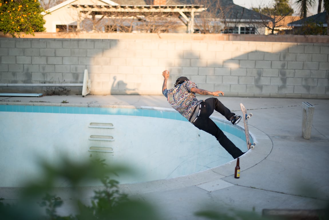 Skateboarder performing a trick in an empty swimming pool during daylight.