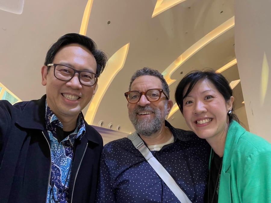 Three people smiling indoors with a modern, curved ceiling in the background.