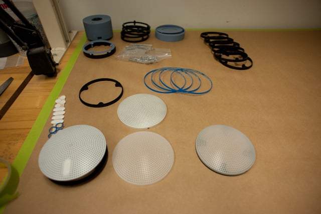 Speaker rings, grilles, and prototype parts arranged on a workbench.