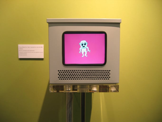 An installation view of Pussy Weevil exhibition showing a monitor with the cartoon character and people interacting with it.