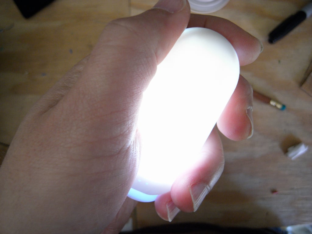 Close view of the smaller Kombolói glowing white in a palm, with fingers curled around its rounded body.