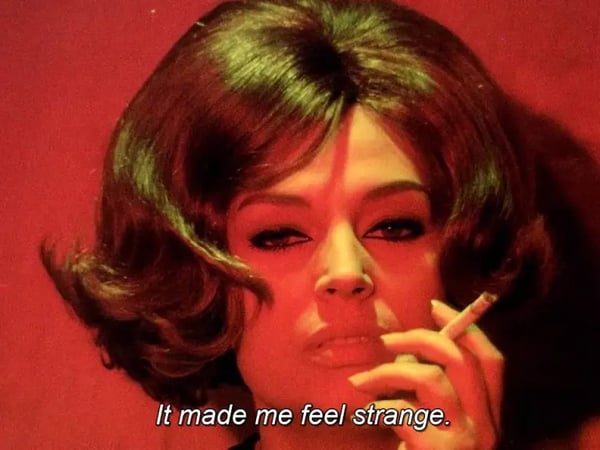 A person with styled hair holds a cigarette against a red background. Subtitles
read, “It made me feel strange.”