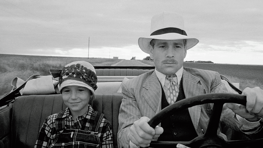 Black-and-white Paper Moon film still showing a father and daughter riding together in a convertible with the steering wheel in view.