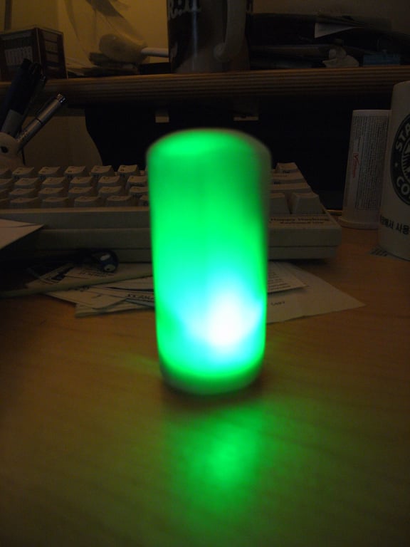 Kombolói standing upright and glowing green on a desk in front of a keyboard.