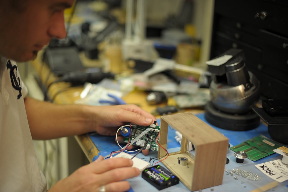 A person touches the rotary-control board beside a wooden Humbo enclosure with loose wiring and an external battery holder.