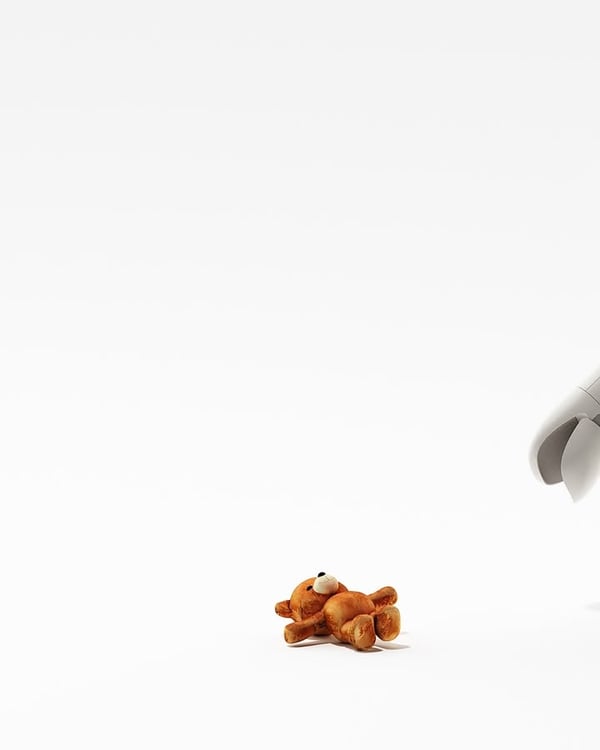 A small teddy bear on a white surface with a robotic hand reaching towards it.