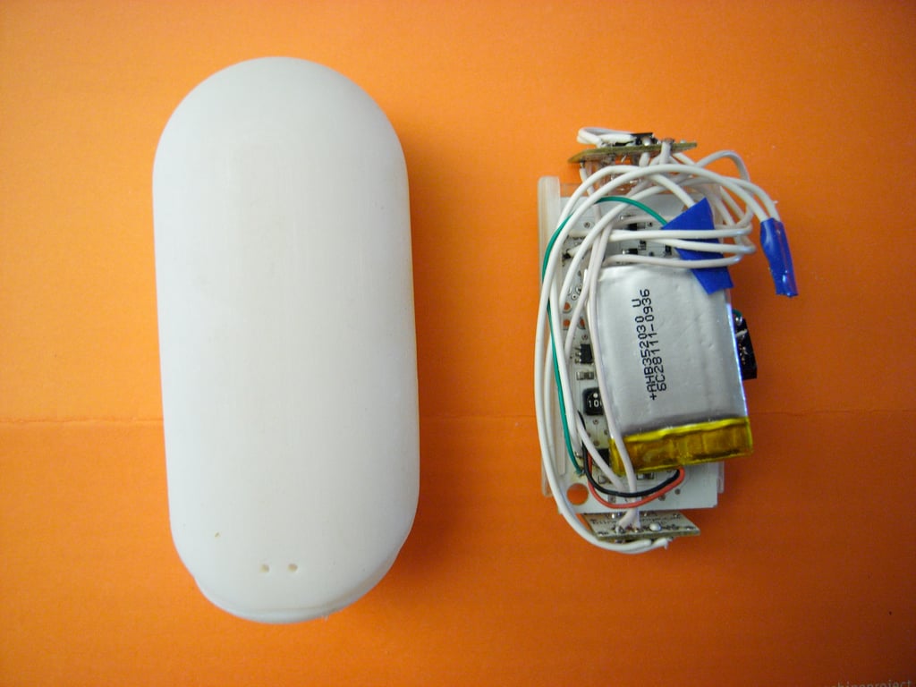 White Kombolói cover beside the exposed battery, circuit board, and bundled wiring on an orange surface.