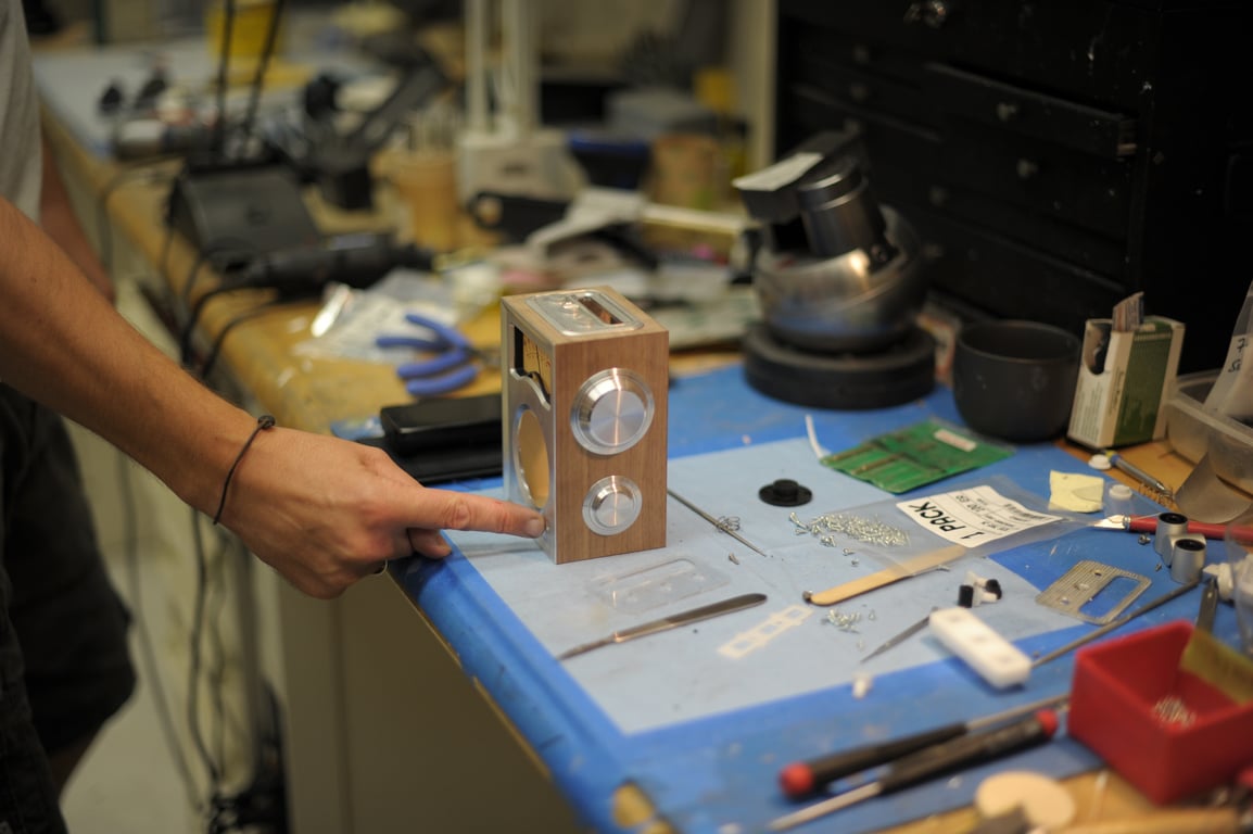 A hand points beside a Humbo enclosure standing on a workbench with two metal side dials fitted.