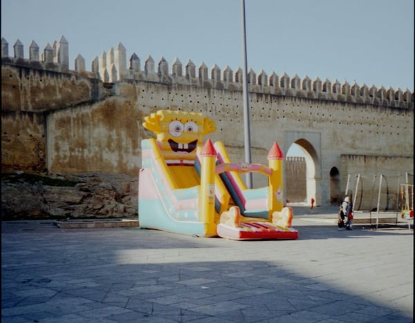 Inflatable slide with cartoon face in front of an ancient stone wall and archway.