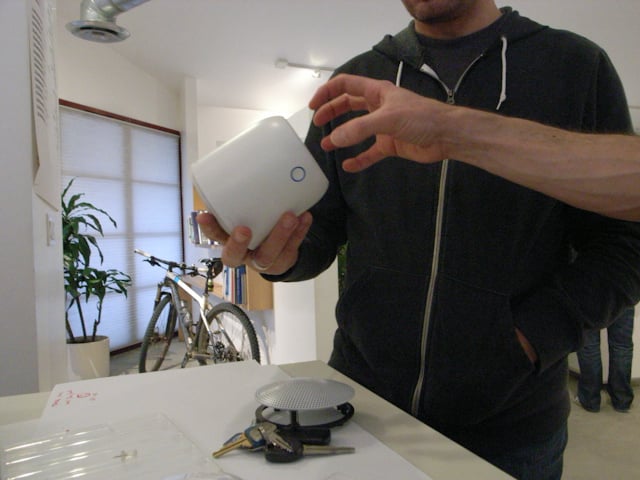 A person holds the white Social Speaker prototype with its top grille lifted to reveal the interior.