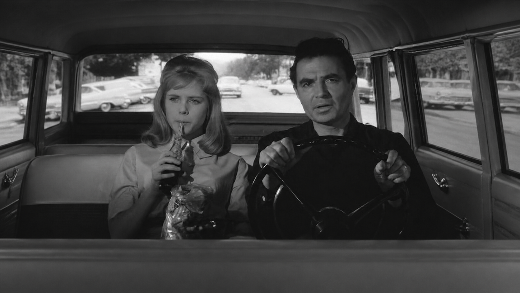 Black-and-white film still from Lolita showing Lolita seated beside Humbert Humbert in a car.