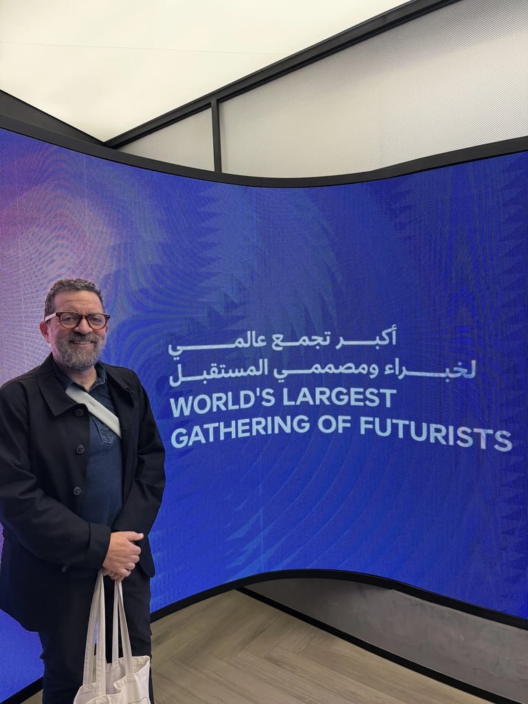 Man smiling in front of a curved screen displaying "World's Largest Gathering of Futurists" in English and Arabic.