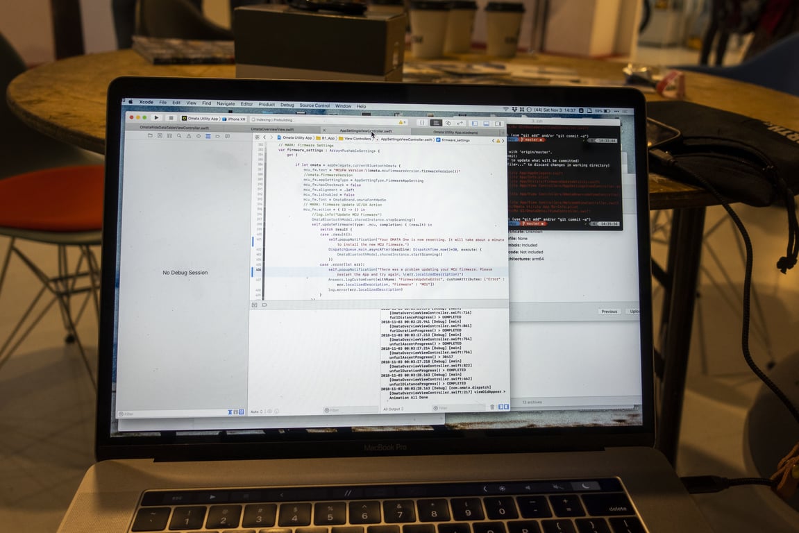 Source code and a terminal window on a laptop at a café table.