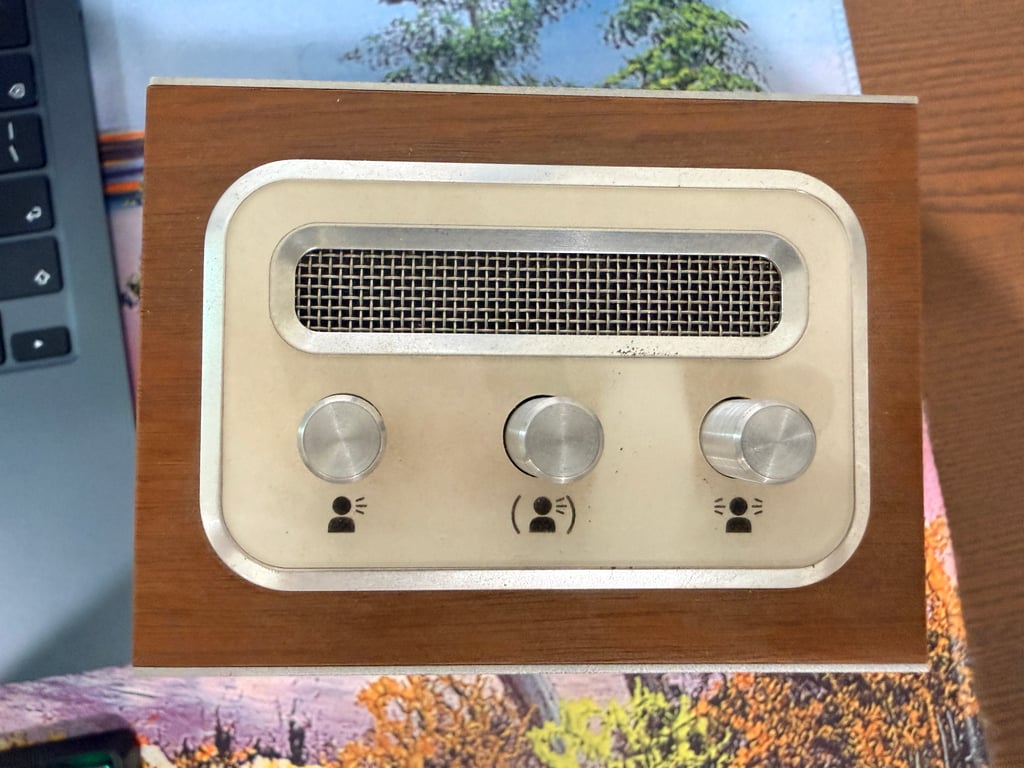 Overhead view of the Humbo top panel with three metal knobs, small person symbols, and a rectangular mesh opening set into wood.