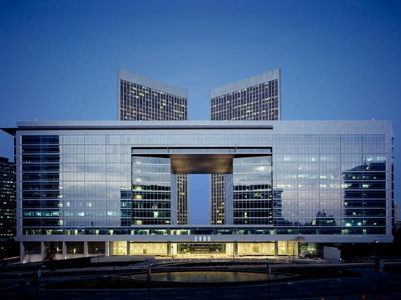 Modern glass Creative Artists Agency headquarters with two towers connected by a central structure, illuminated at dusk.