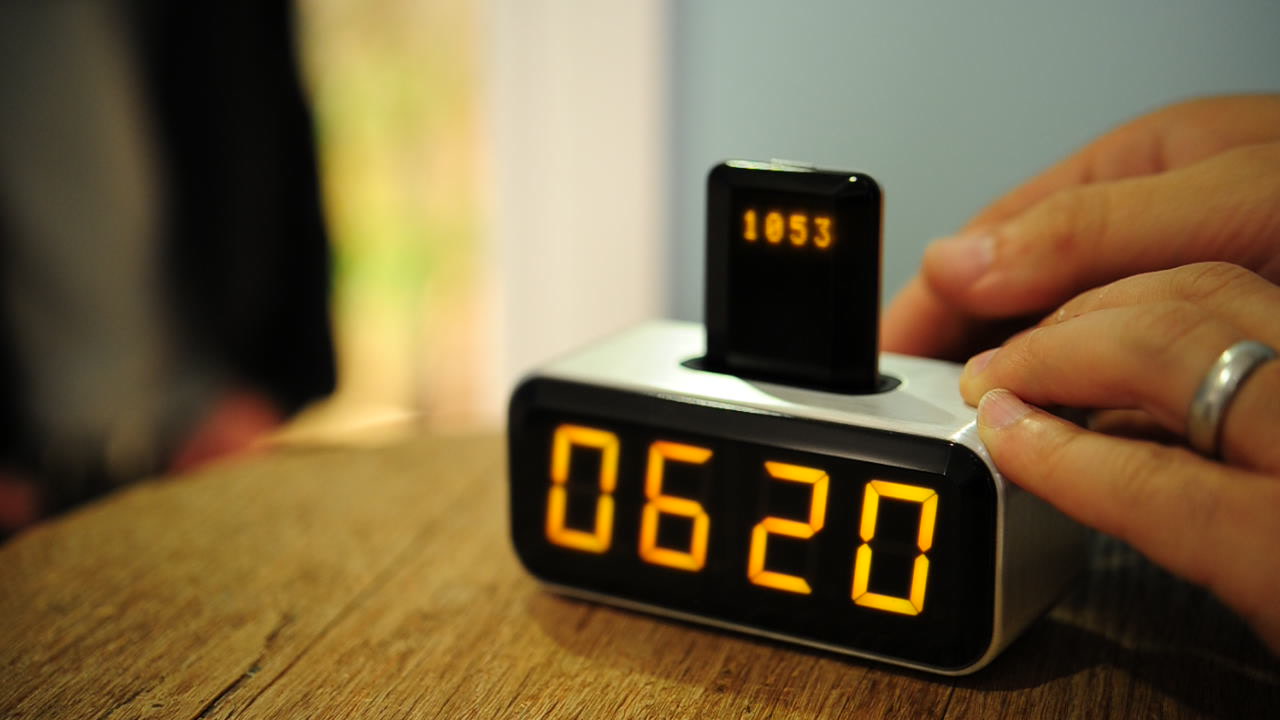 A hand operates the Social Alarm Clock prototype while a docked Nokia phone and illuminated clock display are visible.