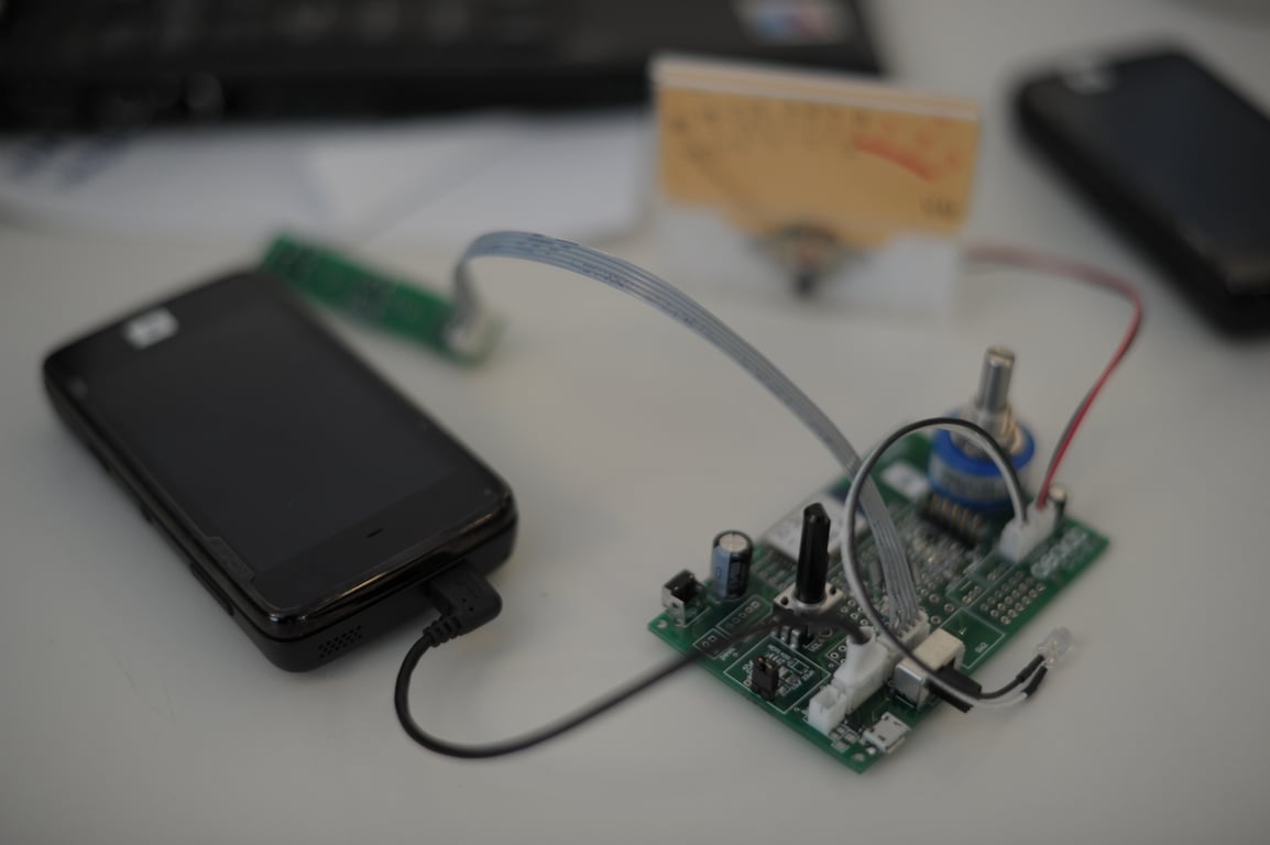 Nokia N900 and custom green circuit board connected by cables, with a blue rotary control and an analog meter behind them.