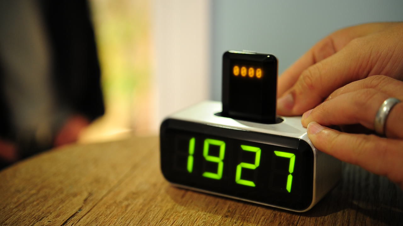 The assembled Social Alarm Clock prototype on a wooden table, with a Nokia phone docked in the top and the clock display illuminated.