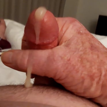 A thick, veiny cock covered in cum, with hairy pubic hair.