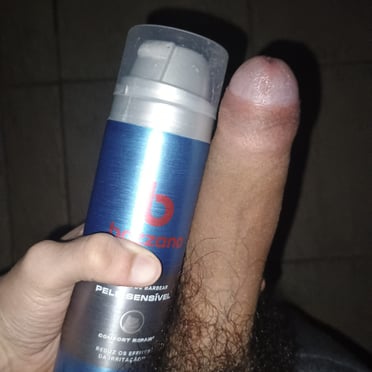 A thick, veiny cock with a full bush of pubic hair is held next to a grooming product, classic Brazilian pics.