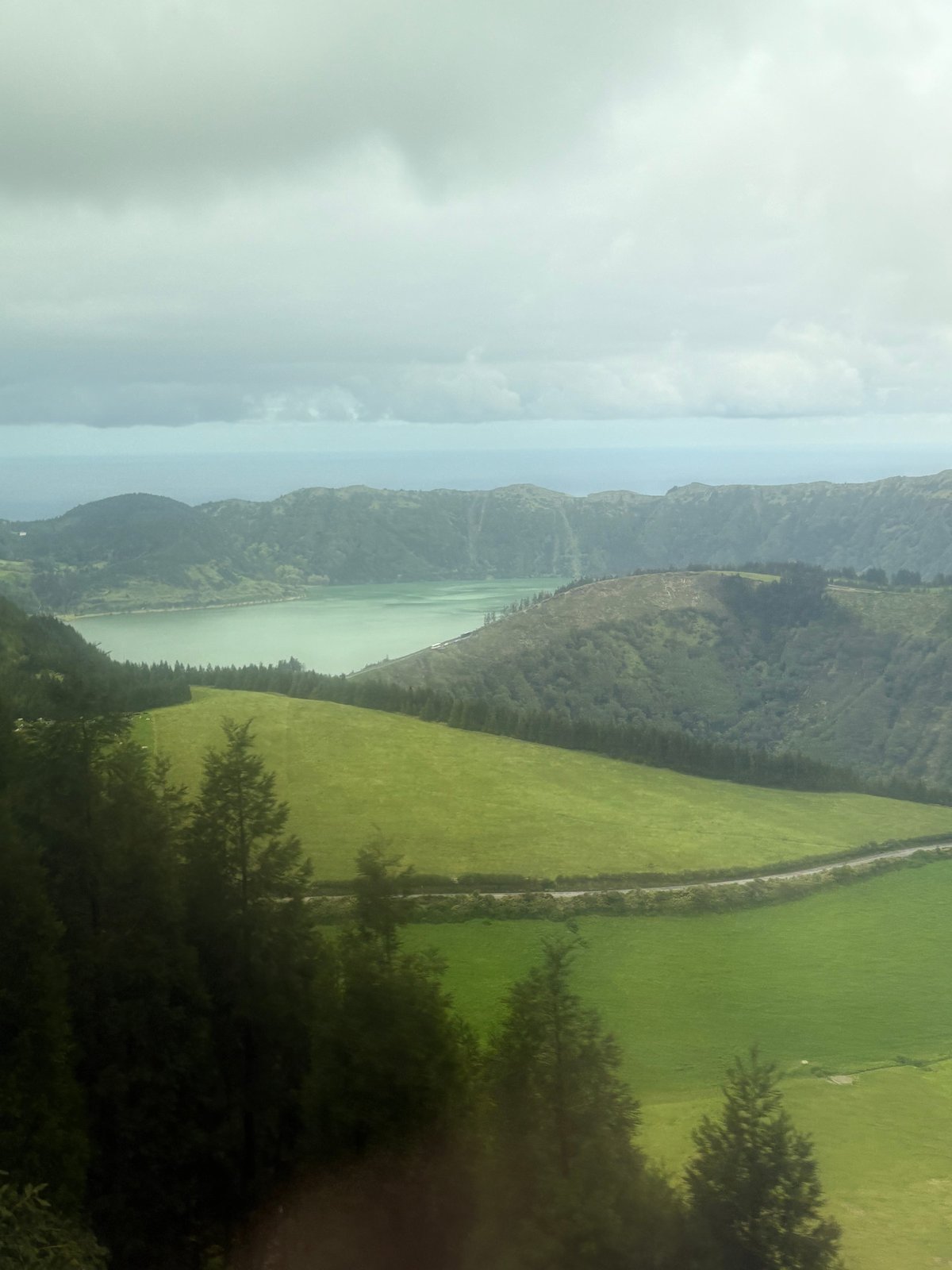 Aerial view of a turquoise crater lake nestled in lush green volcanic hills under a cloudy sky.