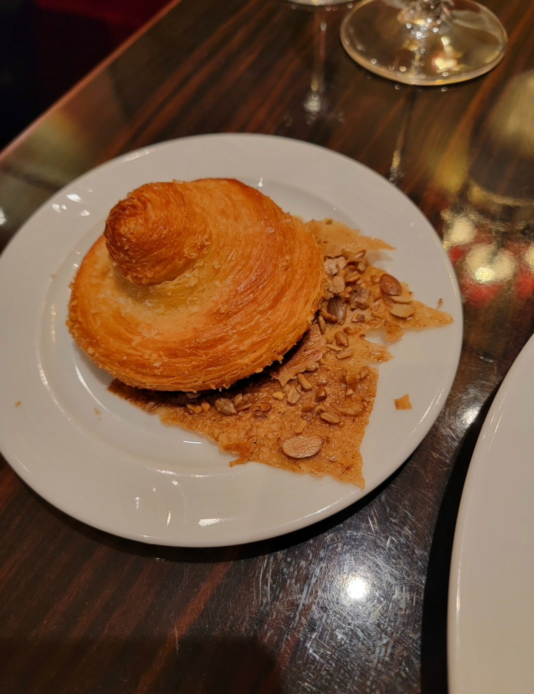 A plate with a spiral pastry and almond-topped baked good on a wooden table with a glass of beverage.