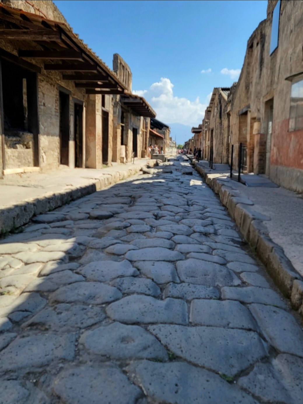 Ancient Roman stone street lined with weathered ruins and columned structures under a clear blue sky.