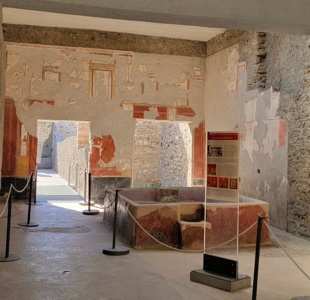 Ancient Egyptian tomb chamber with faded hieroglyphic reliefs and murals on plaster walls, protected by rope barriers and interpretive signage.