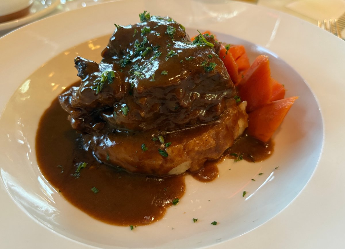 A plated beef dish with rich brown gravy, served over a golden pastry base with roasted red pepper garnish.