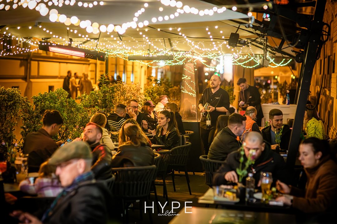 Lively outdoor dining area with people enjoying meals under string lights