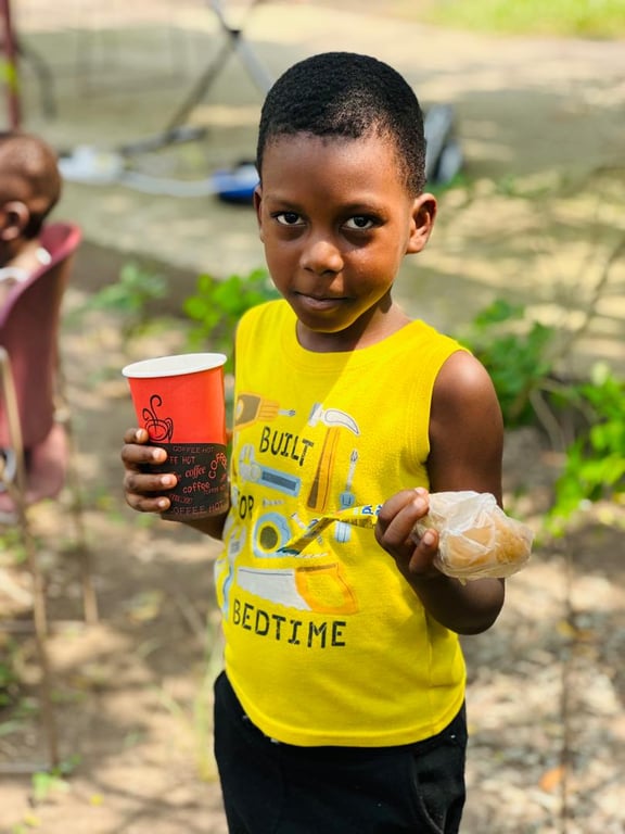 A young boy in a yellow top holding a cup and a snack