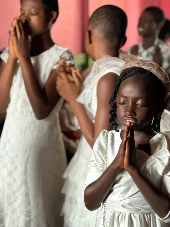 Children dressed in white praying with hands folded during a service