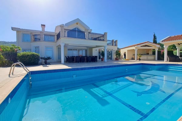 View down lap pool lane showing blue mosaic tiling, ambient lighting, and spacious covered terraces along the villa’s full width.
