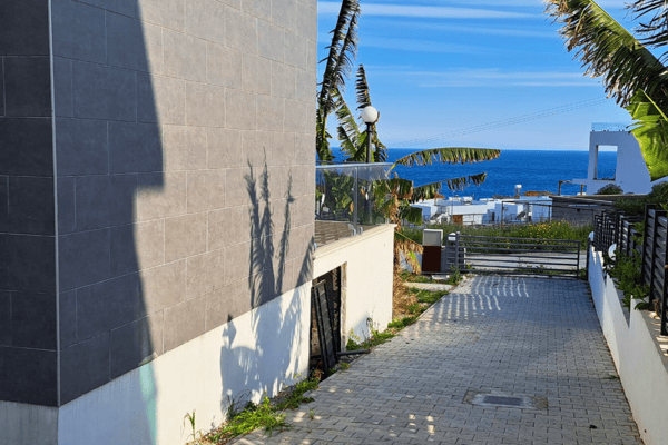 Private driveway flanked by garden walls, opening to a dramatic ocean view that emphasizes exclusive coastal access.