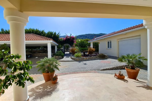 Spacious entry forecourt beneath port-cochère pergola, finished with paving and space for multiple arriving vehicles.