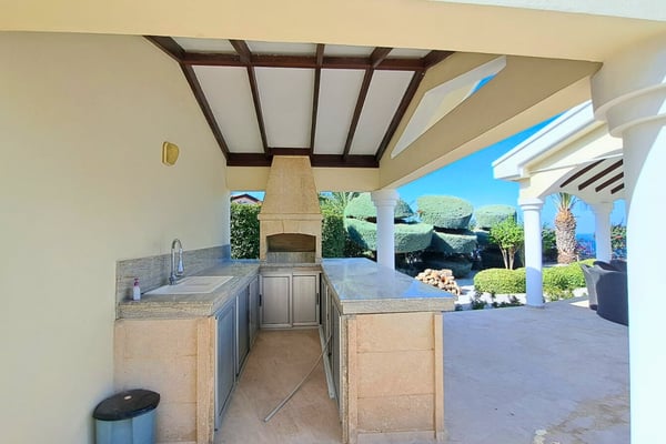 Open-air summer kitchen beneath a pergola, featuring marble counters and tiled splash-back for seamless outdoor hosting.