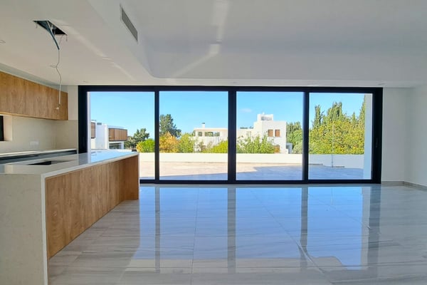 Open-plan kitchen and dining area with white countertops, wood cabinets, and sliding doors opening to the sunny poolside.