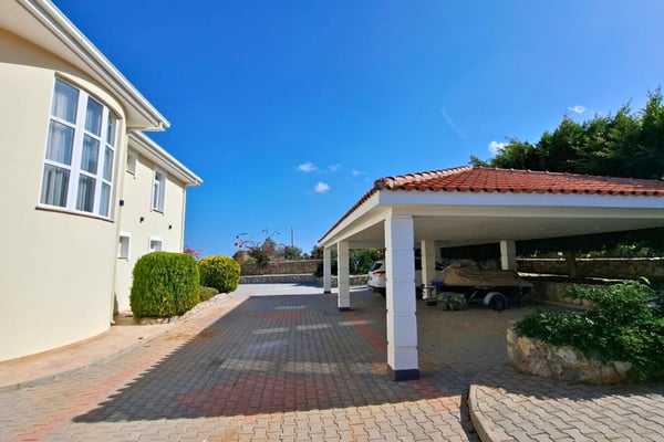 Clay-paved driveway and timber-roofed carport introduce a welcoming entrance framed by stone walls and landscaped detail.