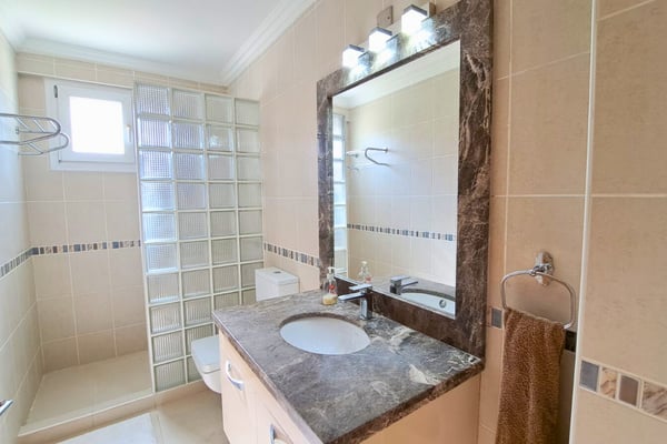 Main bathroom with picture window above tub and dual vanity, blending function with luxurious materials.