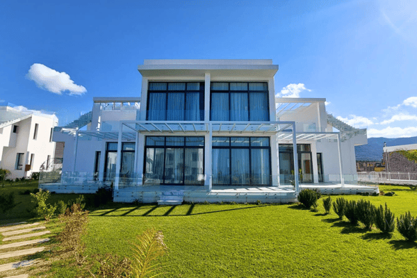 Front view of white geometric villa framed by lush greenery and open glass doors, blending luxury with natural elegance.