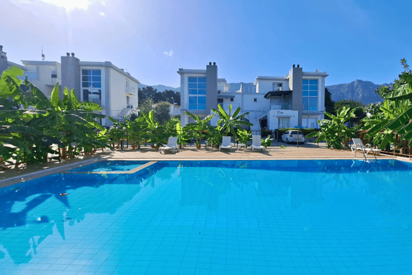 Scenic view from inside a turquoise infinity pool with modern apartments and mountain backdrop, radiating calm and sophistication.