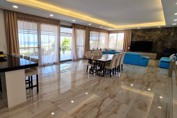 Turquoise pool of a luxury sea-front villa in Northern Cyprus, surrounded by sun loungers, palm trees, and contemporary outdoor furniture.