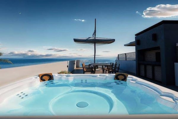 Elevated view of rooftop jacuzzi and lounge furniture with scenic ocean and greenery backdrop enhancing outdoor leisure appeal.