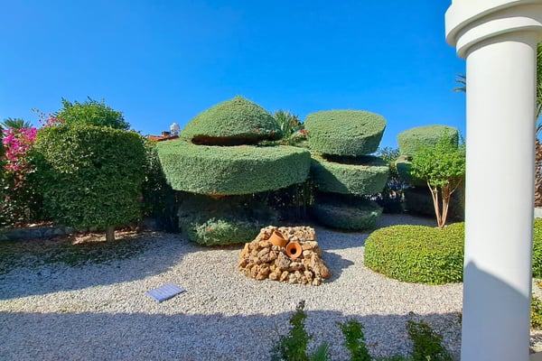 Topiary garden centerpiece with sculpted shrubs, white column, and pebble motif, adding classical flair to the formal grounds.