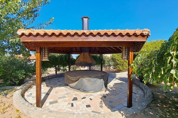 Circular gazebo BBQ shelter with tile roof and gravel surround, ideal for relaxed cooking and casual entertaining poolside.
