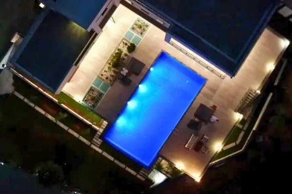 Aerial view of a modern villa with glowing night-lit pool and lush surrounding greenery.