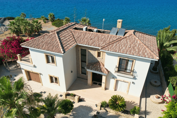 A rear façade view of the villa, showcasing the red-tiled roof, cream walls, and its positioning right above the glistening sea.