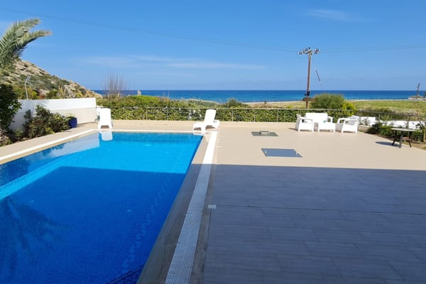 Elegant two-story villa in Esentepe, Northern Cyprus, featuring wraparound glass balconies, floor-to-ceiling windows, and lush tropical greenery.