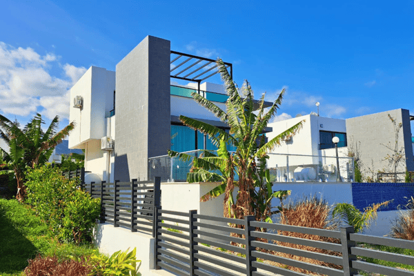 Side view of a contemporary villa framed by tropical greenery and glass balconies that embrace indoor-outdoor harmony.